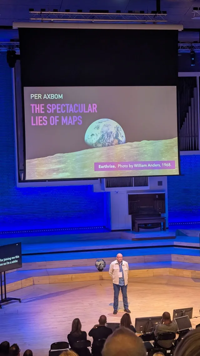 Photo: James Winstone: Per Axbom on stage at Camp Digital 2025. The opening slide: The Spectacular Lies of Maps, with the Earthrise photo.