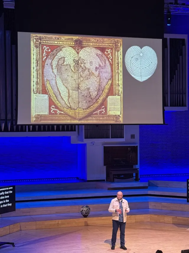 Photo: Joanna Czutkowna: Per Axbom on stage at Camp Digital 2025. A heart-shaped historical world map next to its projection grid.