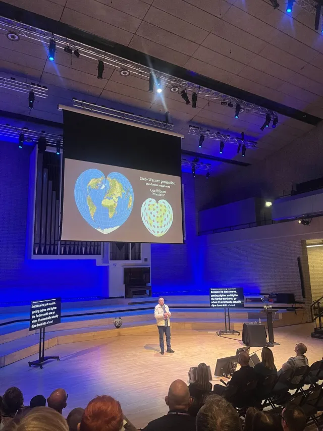Photo: Megan L.: Per Axbom on stage at Camp Digital 2025. Comparing heart-shaped map projections.