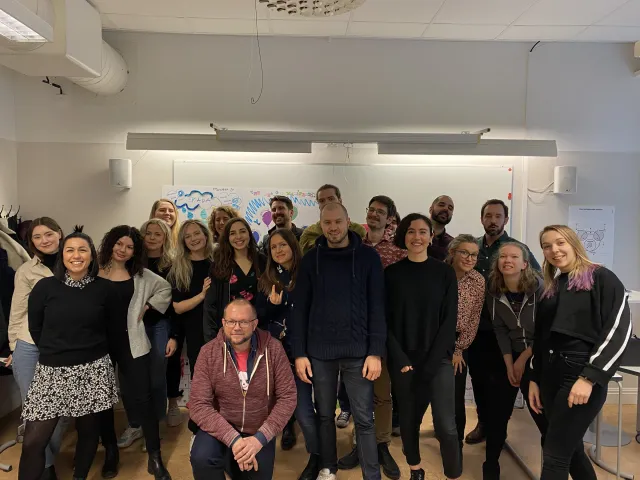 Per kneeling in front of a class of about twenty-five UX students, all smiling, in a classroom with posters on the whiteboard behind them, February 2020.