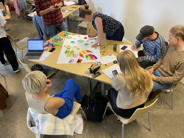Group work, September 2022: Students around tables covered in paper, colored markers and sticky notes, working on a large poster.