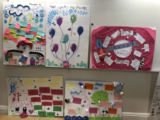 Manifestos on the wall, February 2020: Several student manifestos hang together: balloons, sticky notes, drawings and the pink Uranux manifesto.